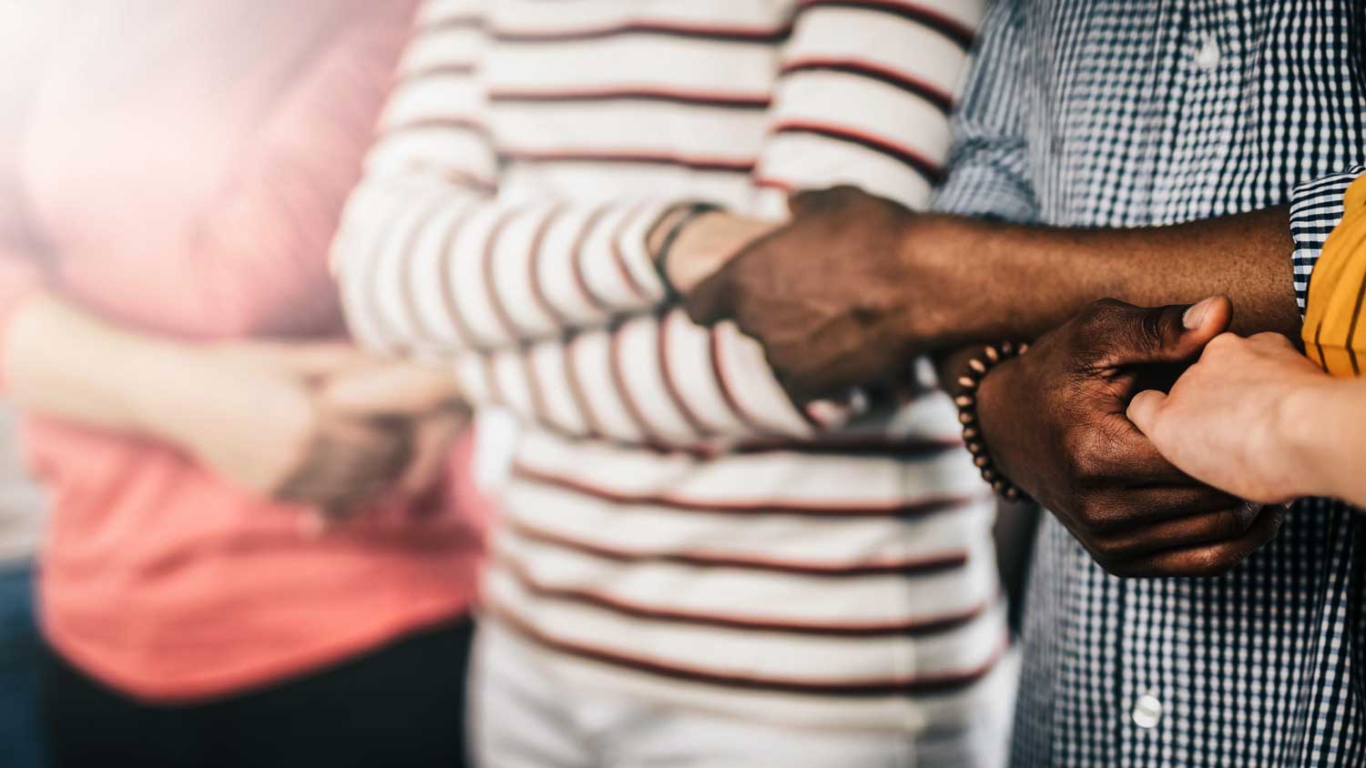 A group of people with linked arms to symbolize team unity