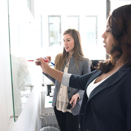 Two businesswomen writing on a whiteboard